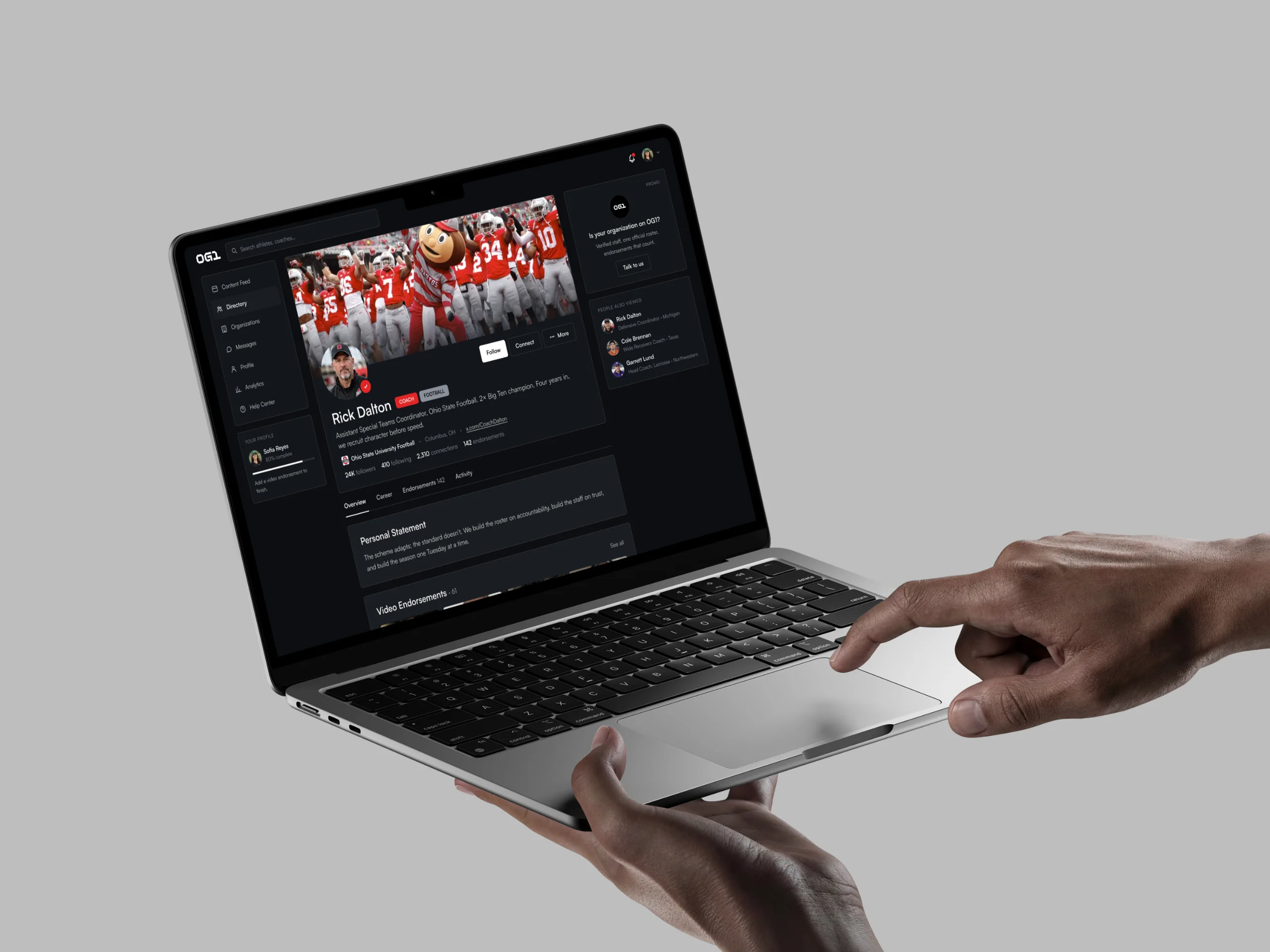 Hands hold a laptop that shows an OG1 coach profile.