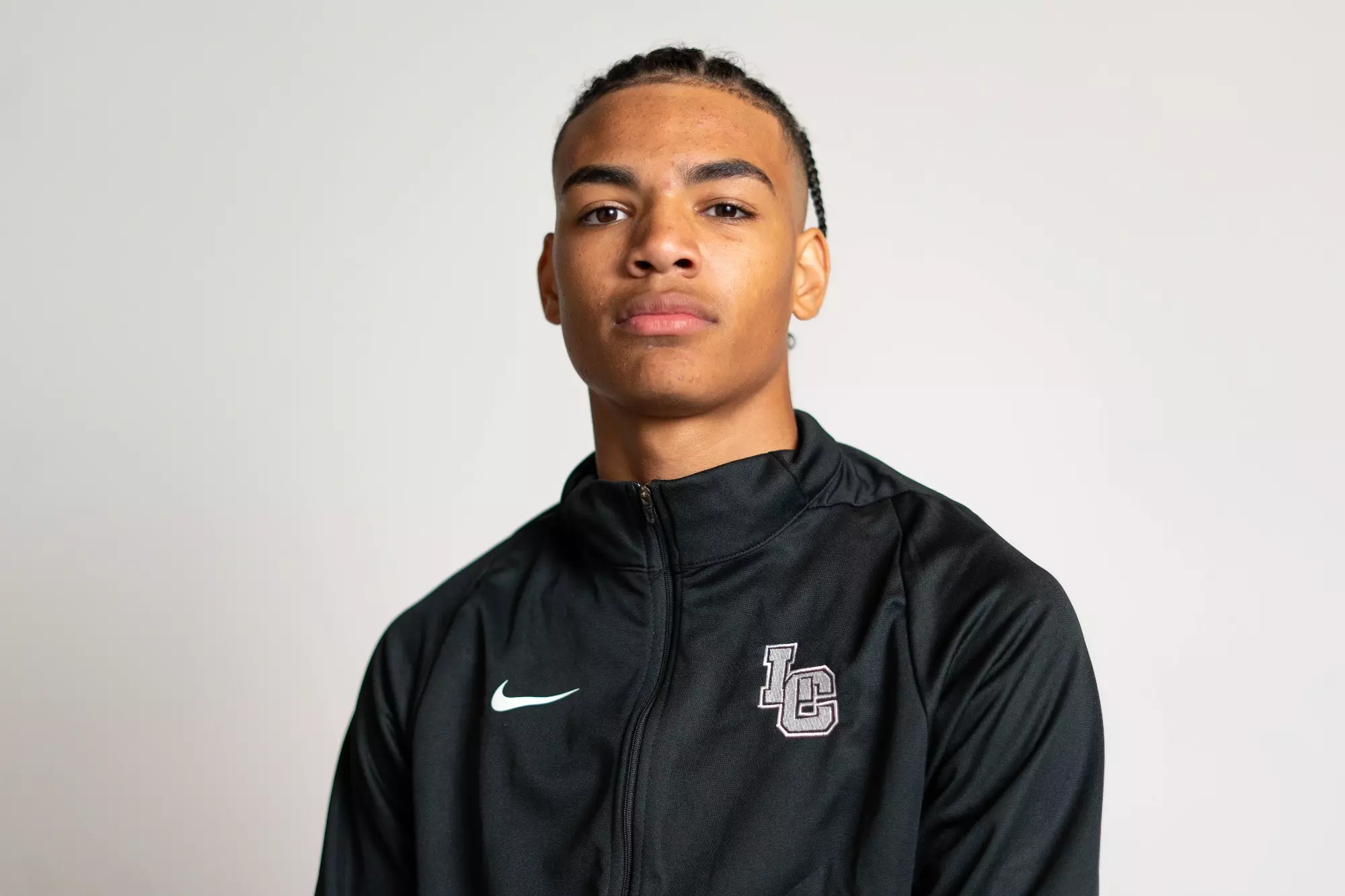 A high school football player in a black team jacket looks at the camera.