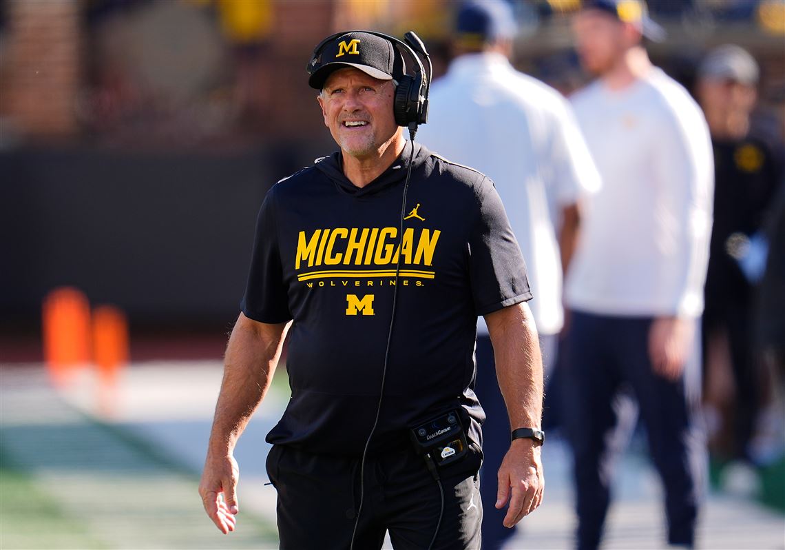 A Michigan football coach on the sideline, wearing a headset.